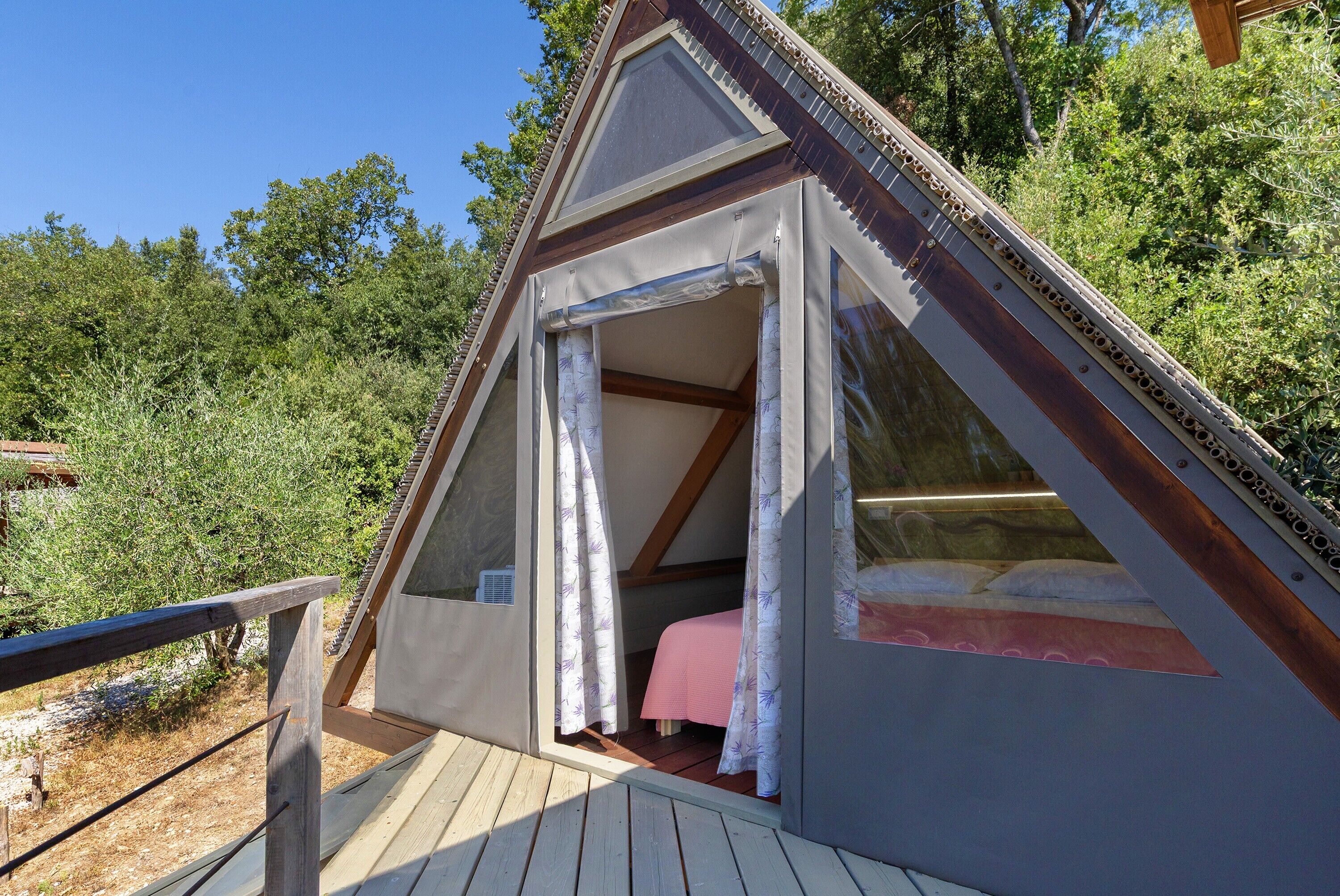 A triangular wooden structure with a bed, a window, and a door.