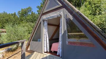 A triangular wooden structure with a bed, a window, and a door.