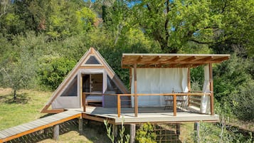 A small, triangular wooden structure with a balcony, a covered seating area, and a bed inside.