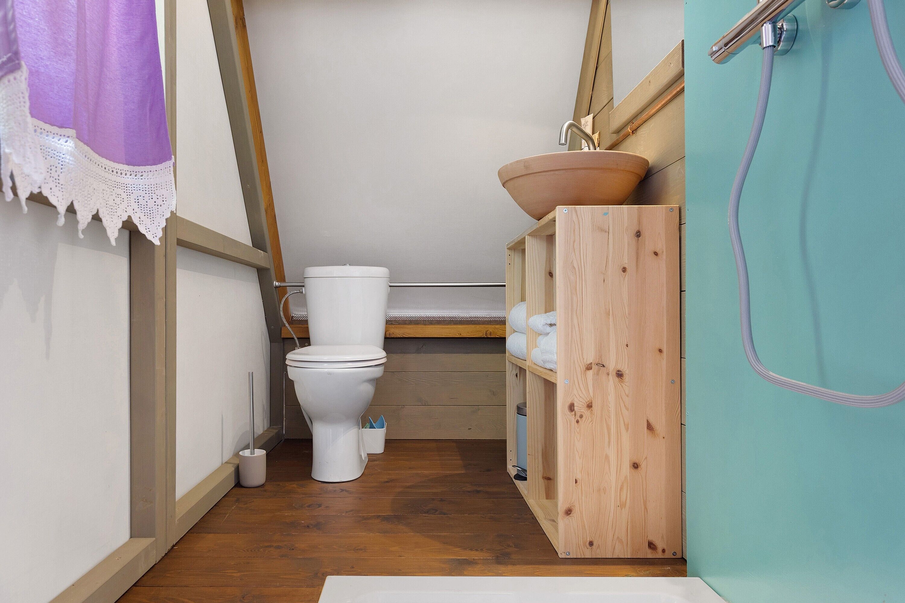 A compact bathroom with a toilet, a wooden shelf with towels, and a shower area.