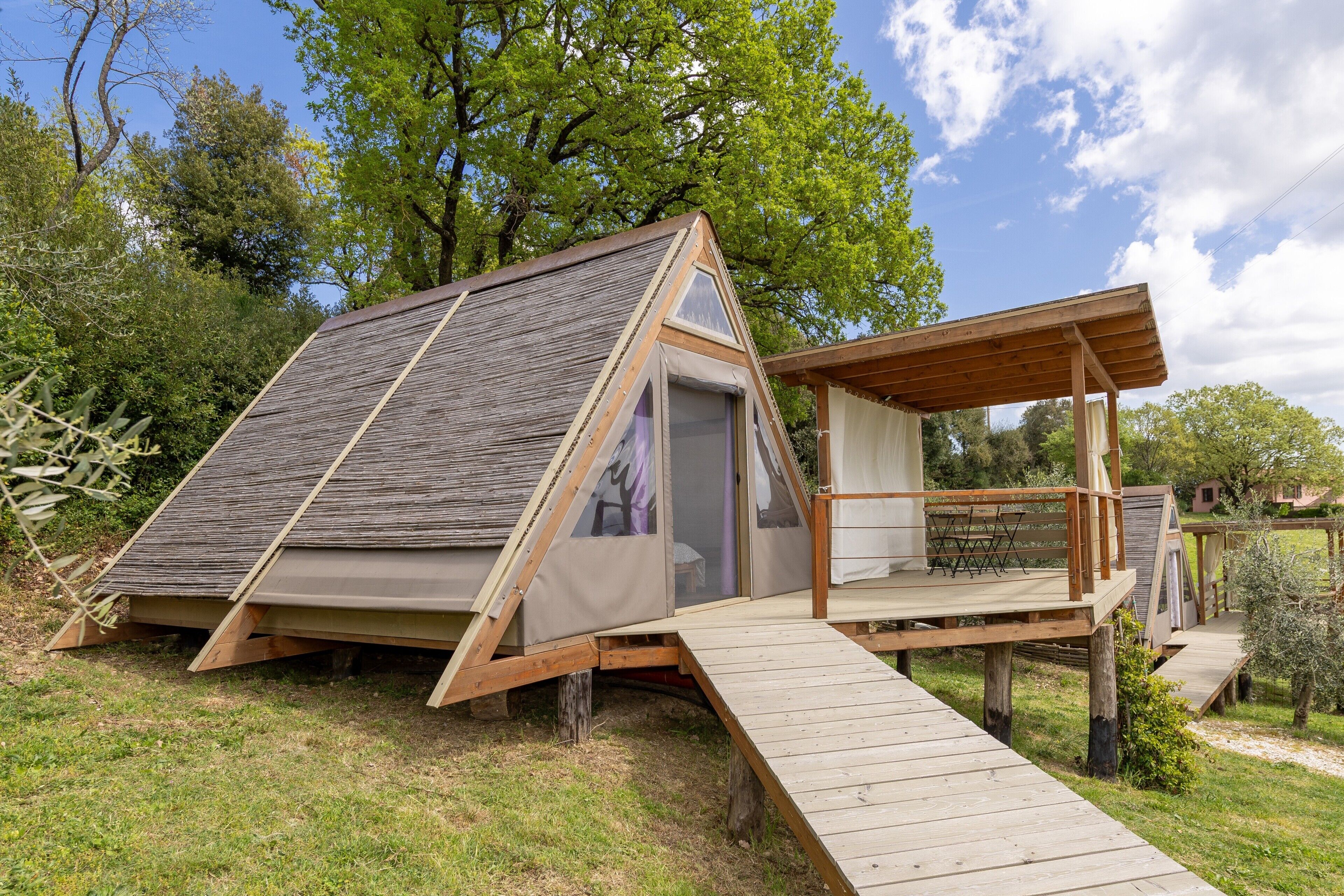 A triangular wooden structure with a deck, a covered area, and a door.