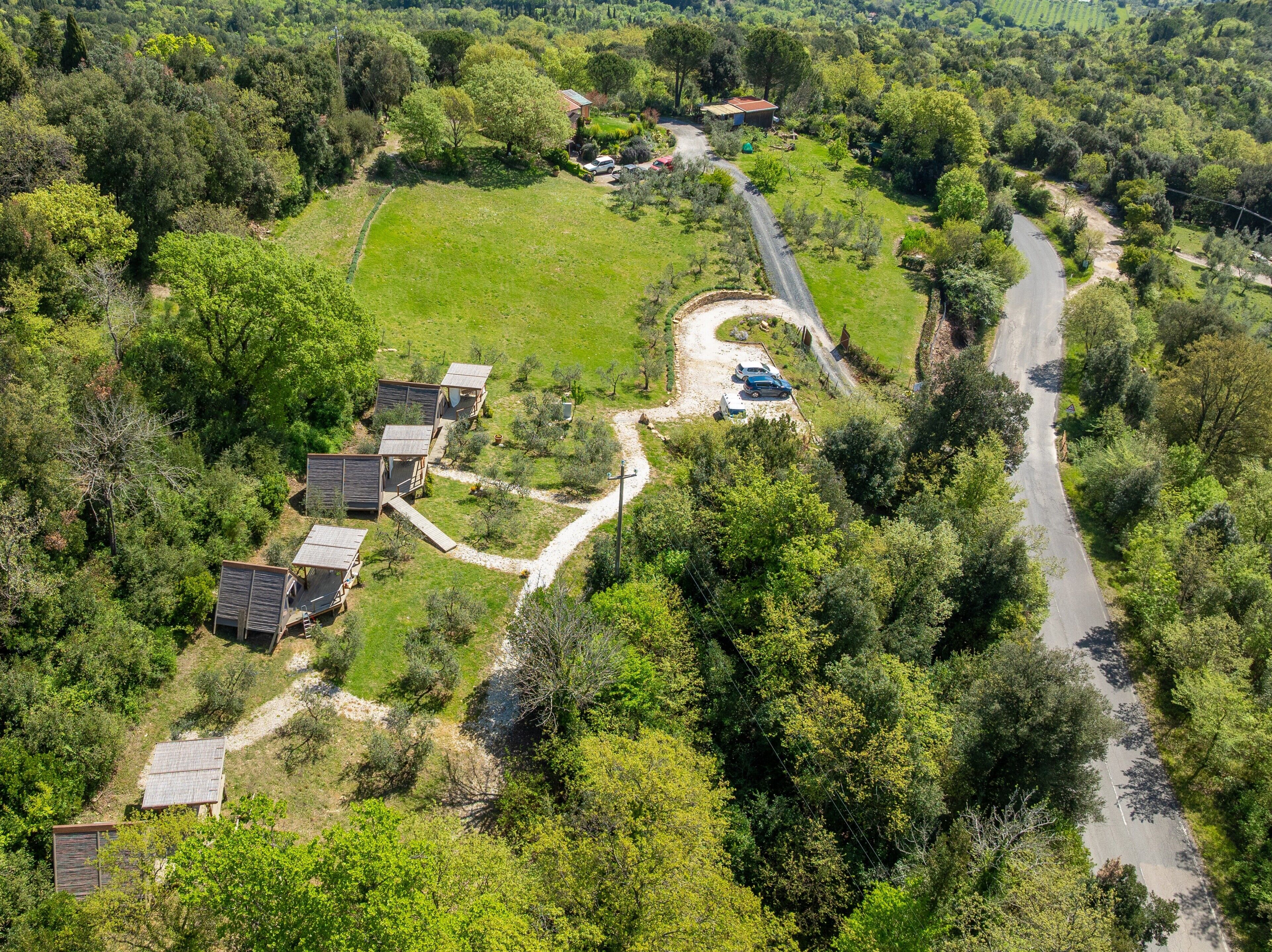 An aerial view of a rural property with several wooden cabins, a winding road, and surrounding greenery.