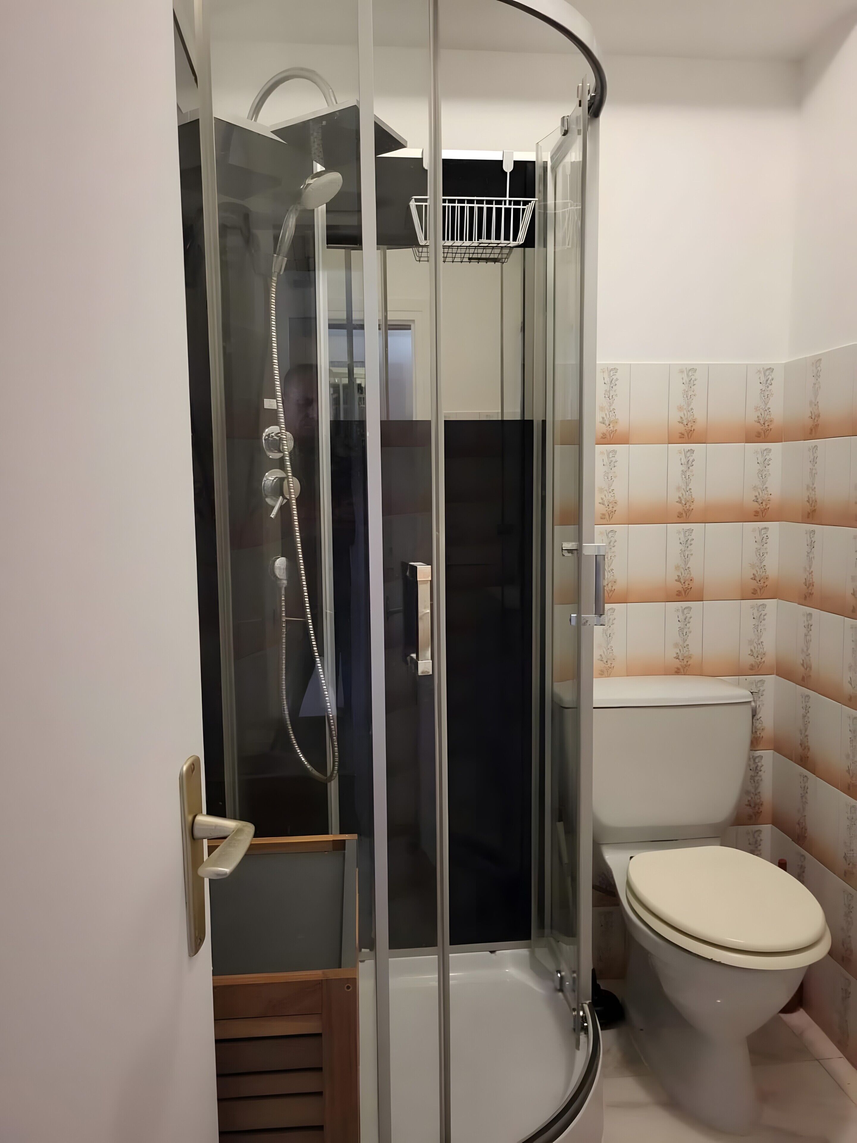 A glass-enclosed shower with a handheld showerhead, a toilet, and a wooden bench.
