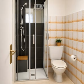 A modern bathroom with a glass-enclosed shower, a toilet, and a small wooden bench. - Apartment 'Cannes Cousin Studio' with Balcony, Wi-Fi and Air Conditioning (Cannes)
