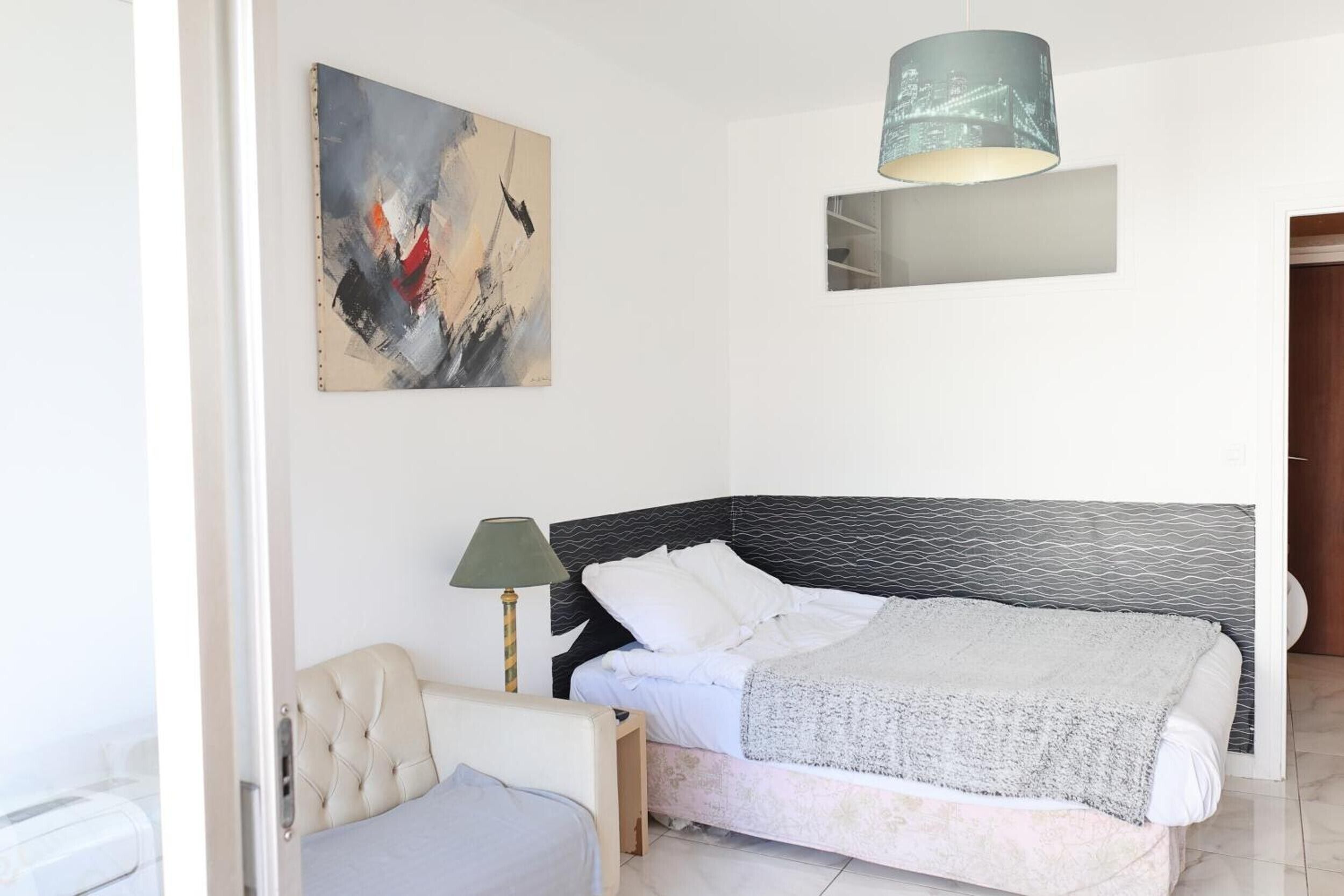 Un dormitorio con cama, una silla, un cuadro y una lámpara.