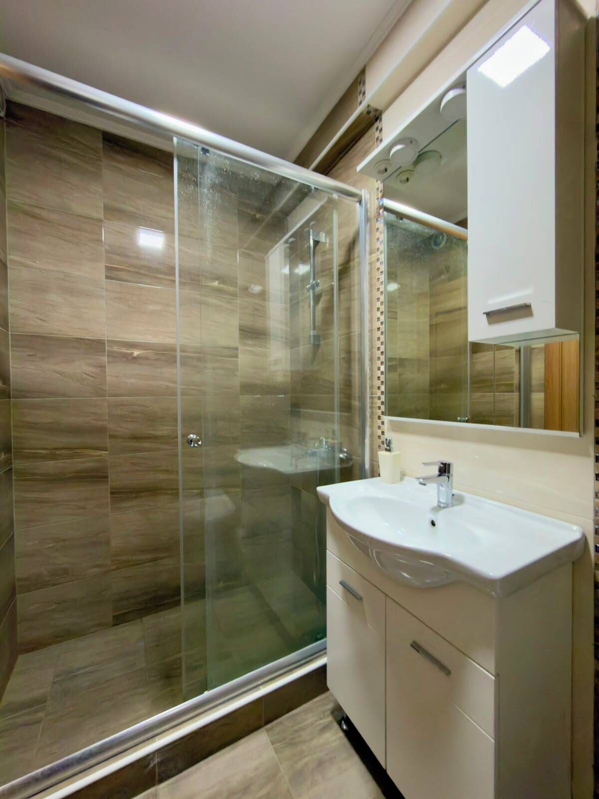 Un baño moderno con ducha envuelta en cristal, un lavabo blanco y un espejo sobre él.