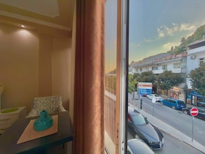A room with a view of a street outside, a table with a tissue box, and a window with curtains.