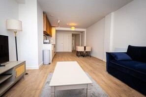 A modern living room with a flat-screen TV, a dark blue sofa, a white coffee table, and a dining area with two chairs and a small table. - Birmingham City Retreat No 111 (Birmingham)