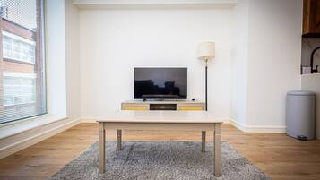 A modern living room with a flat-screen TV on a white stand, a grey carpet, and a lamp on the right.