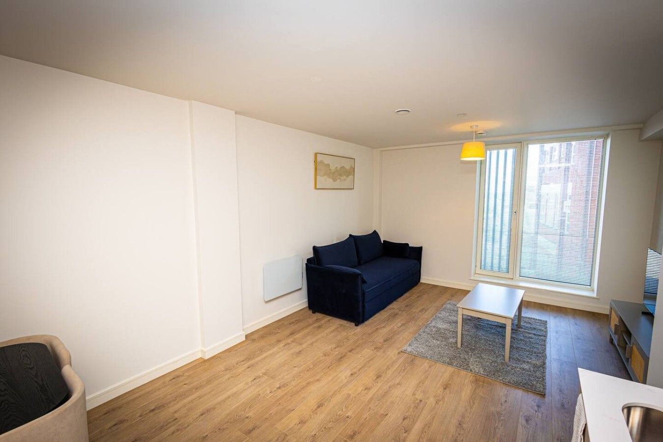 A room with a dark blue sofa, a small table, a radiator, and a window with blinds.