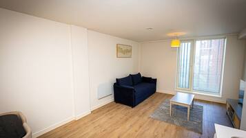 A room with a dark blue sofa, a small table, a radiator, and a window with blinds.