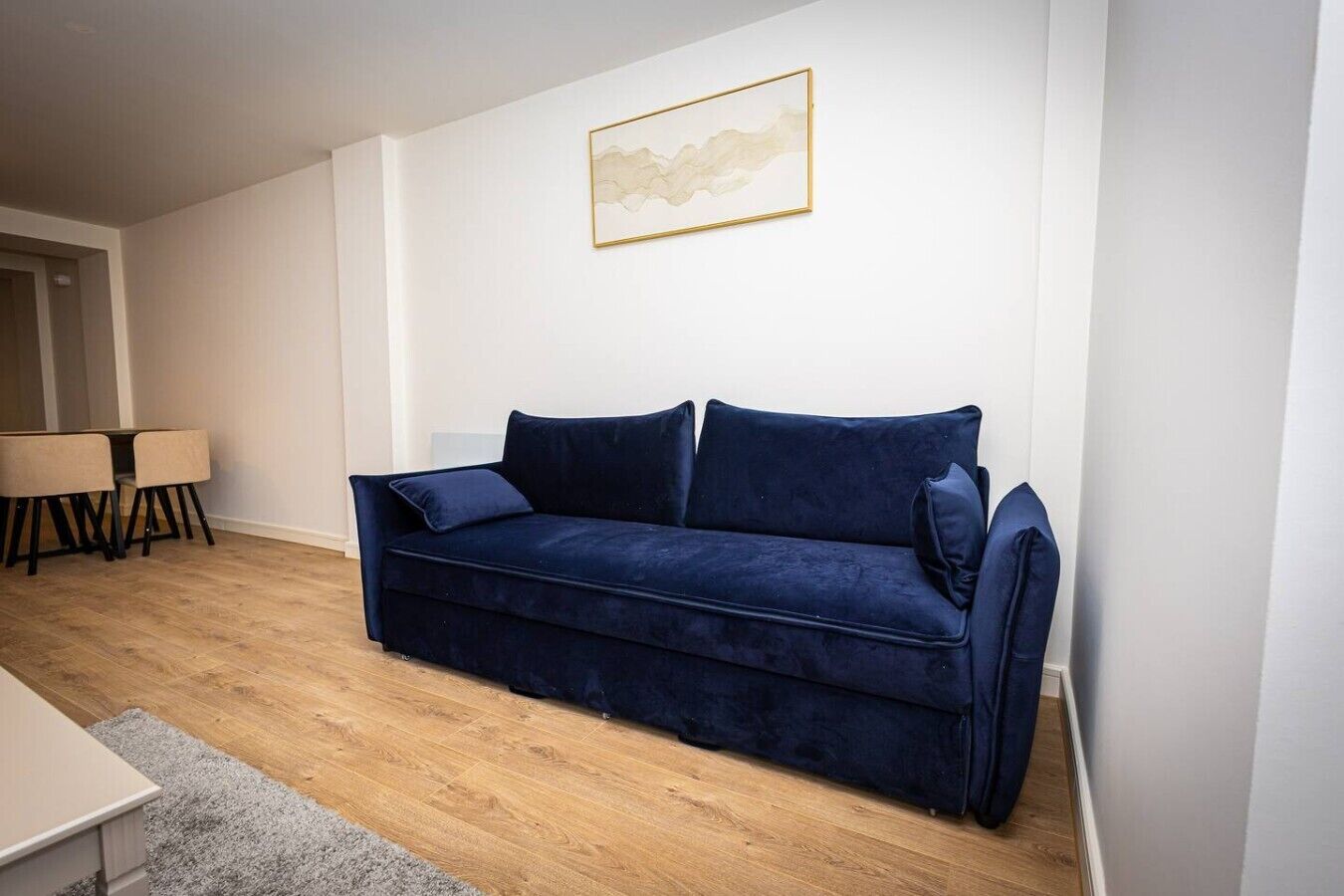 A living room with a dark blue sofa, a small table with chairs, and a framed picture on the wall.