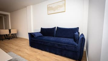 A living room with a dark blue sofa, a small table with chairs, and a framed picture on the wall.