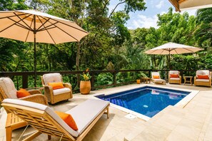 An outdoor pool area with lounge chairs and umbrellas, surrounded by lush greenery. - Private Pool Villa • 2 King Suites • Walk to West Bay Beach (West Bay)