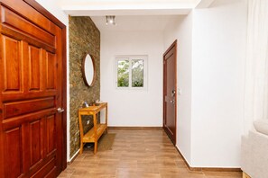 Ein Flur mit einer Holztür, einer Steinwand, einem kleinen Tisch mit Gegenständen und einem Fenster mit Blick auf Grünflächen.