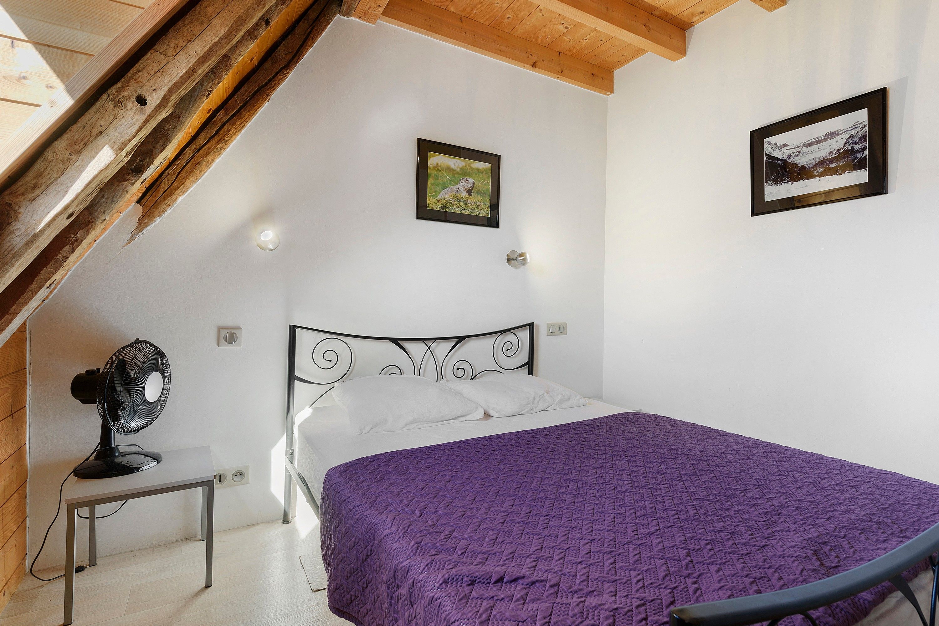 Un dormitorio con una cama, un ventilador, un cuadro en la pared y techo de madera.