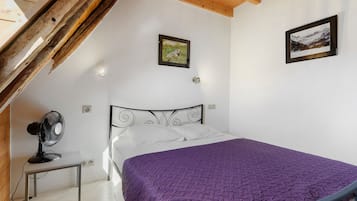 Un dormitorio con una cama, un ventilador, un cuadro en la pared y techo de madera.