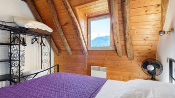 A bedroom with a sloped ceiling, a window with a mountain view, a bed with a purple blanket, and a wall-mounted heater.