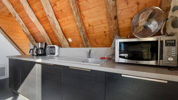 A kitchen with a wooden ceiling, a sink, a microwave, and a kettle on the counter.