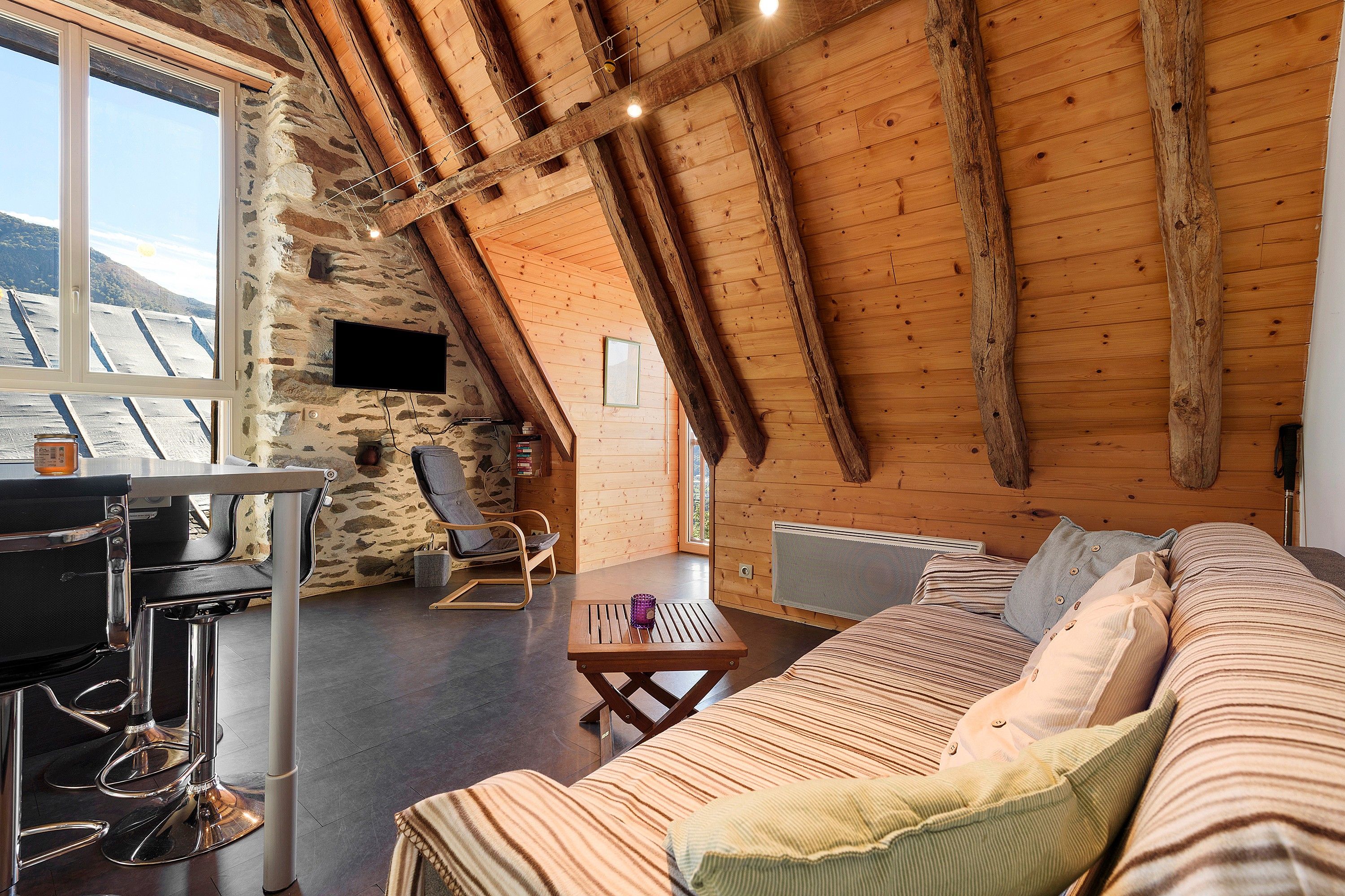 Ein gemütlicher Loft-Raum mit Steinwand, Holzbalken, einer Couch, einem Tisch und einem Sessel.