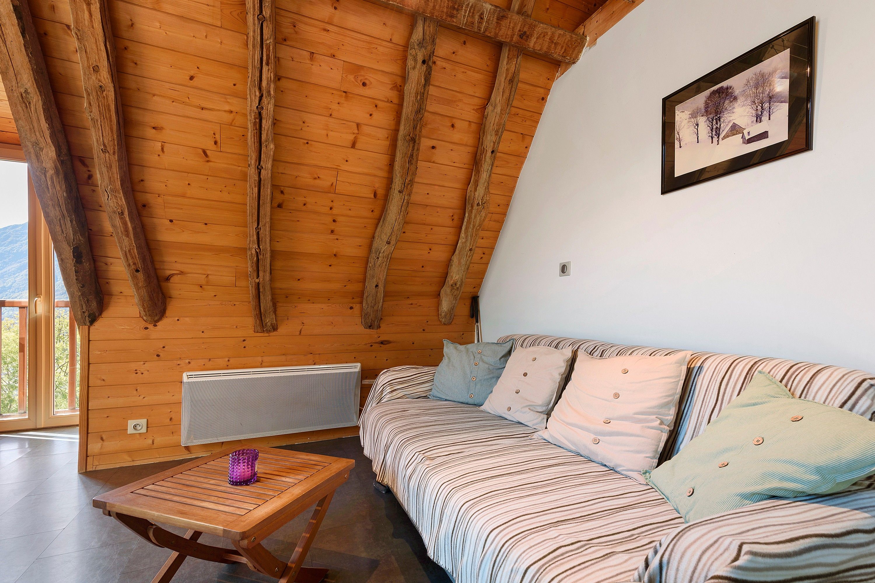 Una habitación acogedora con techo de madera inclinado, un sofá a rayas y una pequeña mesa con un objeto morado.