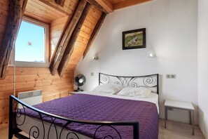 A bedroom with a sloped ceiling, a bed with a purple blanket, a small bedside table, a wall-mounted picture, and a window with a view of the sky. - "La Grange" Gîte with Mountain View and Wi-Fi (Artalens-Souin)