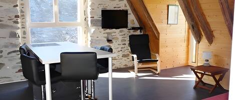 Une pièce avec un mur en pierre, une table blanche avec des chaises, un téléviseur et un canapé rouge.