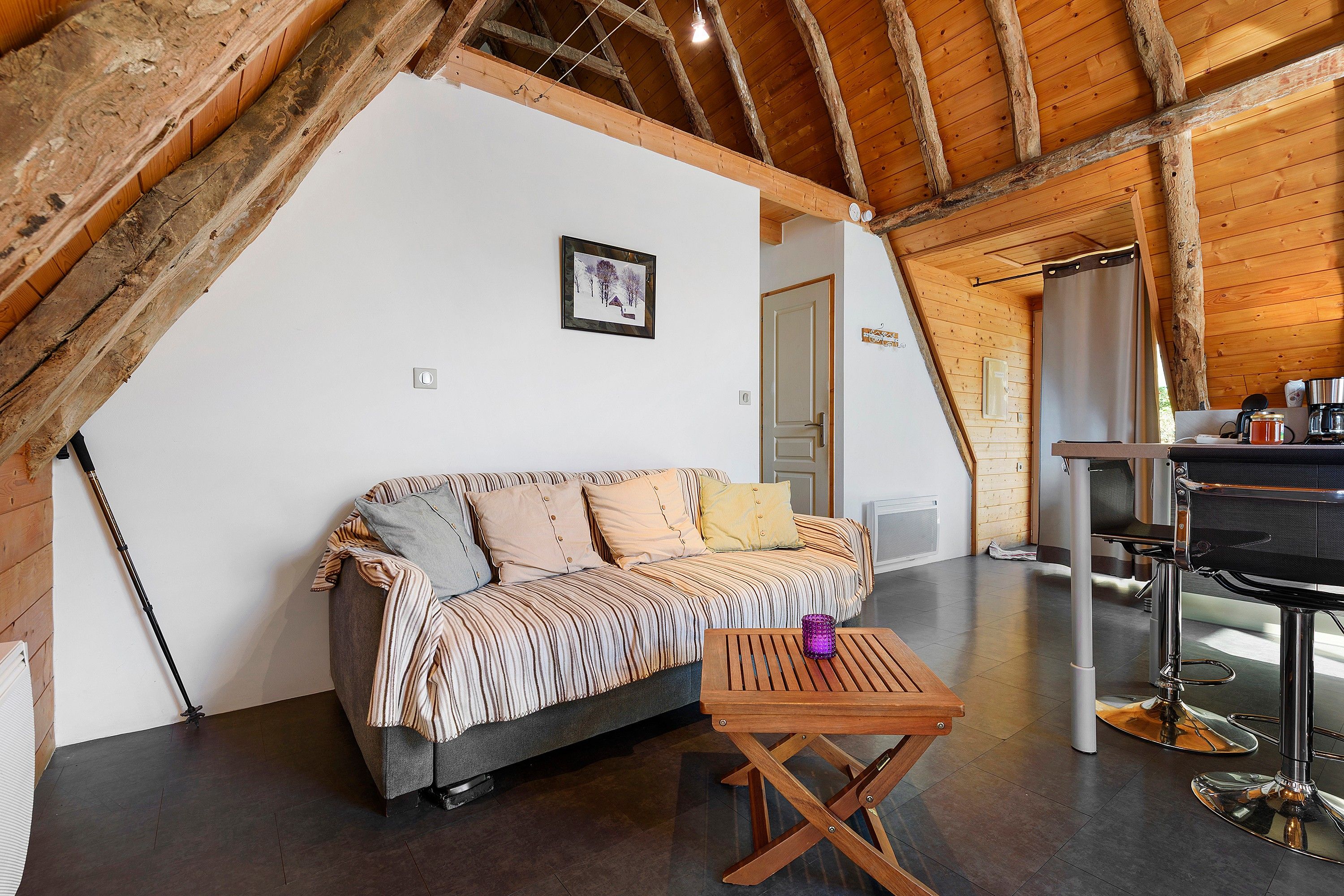 Una habitación acogedora con techo de madera, un sofá con cojines a rayas, una pequeña mesa de madera y una zona de bar con cafetera.