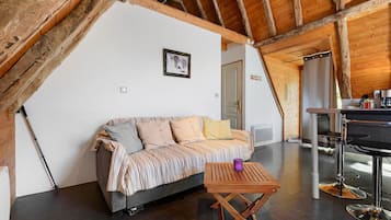 Una habitación acogedora con techo de madera, un sofá con cojines a rayas, una pequeña mesa de madera y una zona de bar con cafetera.