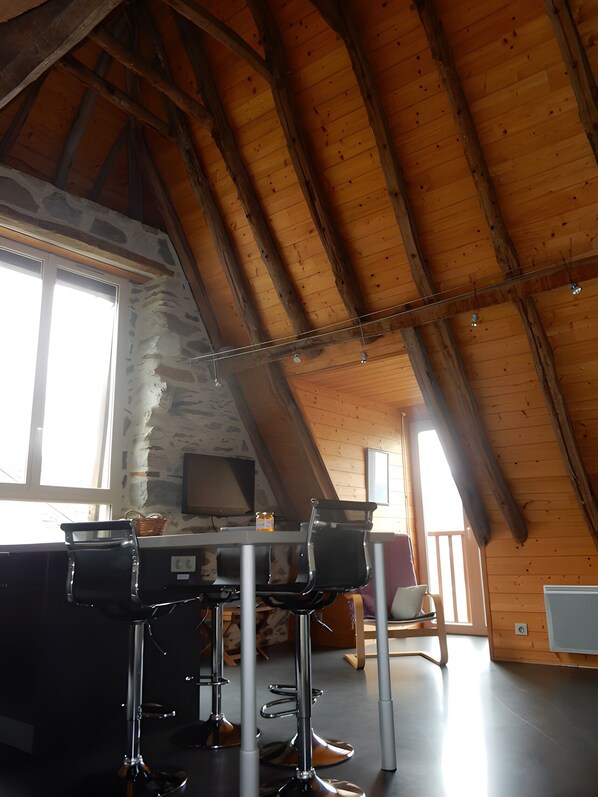 A rustic interior with a sloped ceiling, a stone wall, a wooden table, and two bar stools.