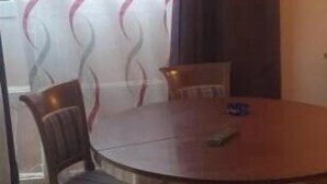 Een ronde houten tafel met vier stoelen, een raam met gordijnen, en een houten plafond.
