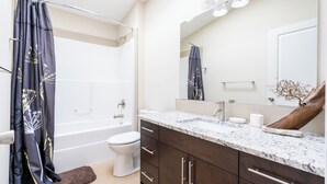 Une salle de bain moderne équipée d’une baignoire, de toilettes, d’un meuble-lavabo et d’un grand miroir.