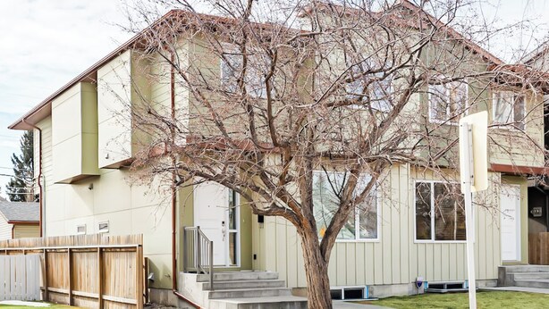 Une maison à deux étages avec un jardin devant, une clôture en bois et un arbre.