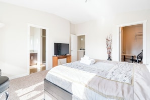 Ein modernes Schlafzimmer mit einem großen Bett, einem Fernseher, einem Schreibtisch und einem Sessel.