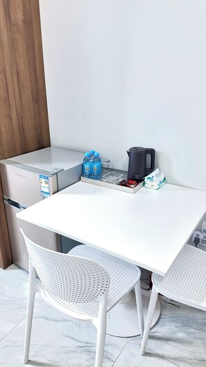 Una mesa blanca con una tetera, botellas de agua y una bandeja con bocadillos.