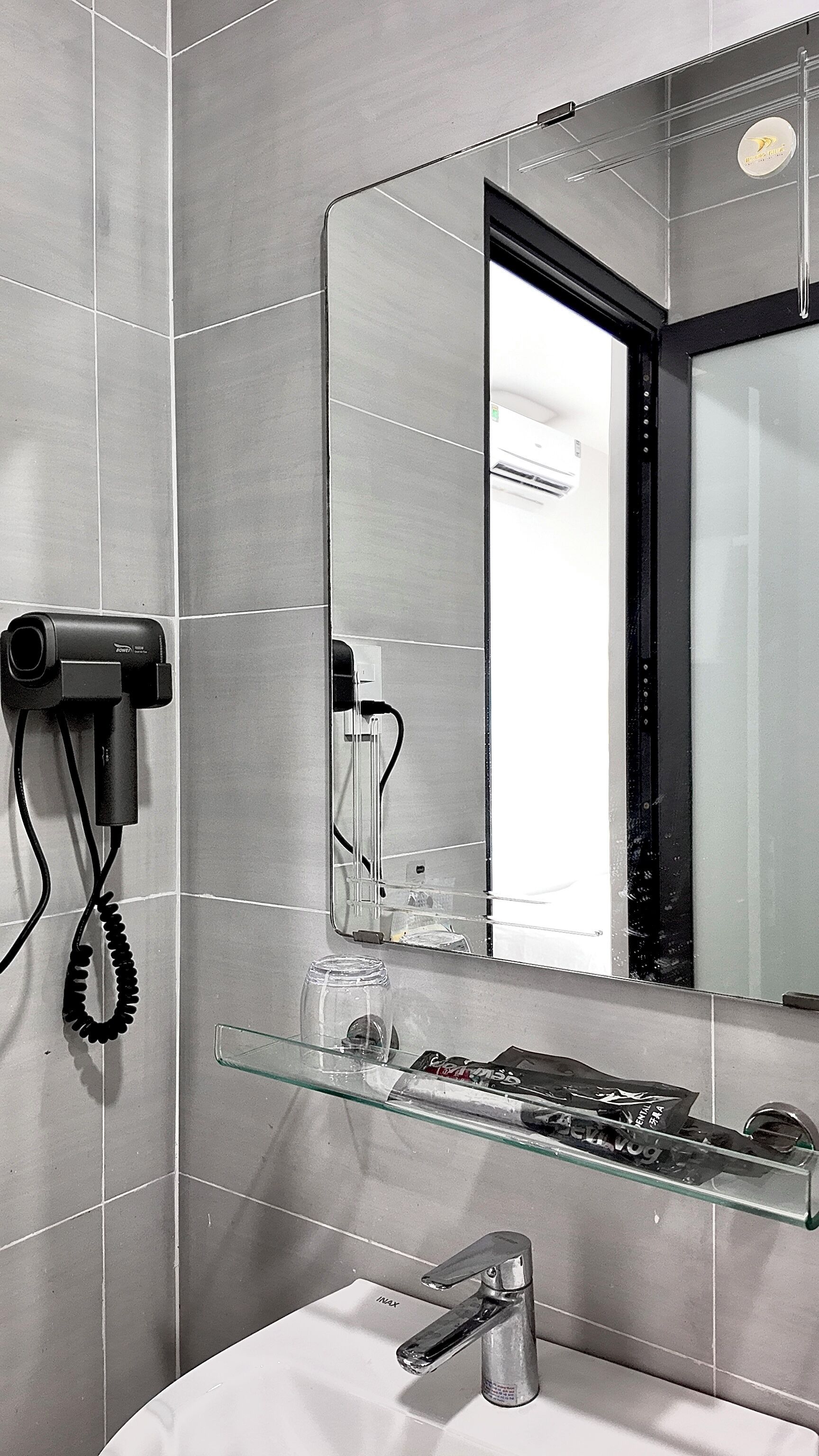 A bathroom with a glass shelf, a sink, a mirror, and a hairdryer mounted on the wall.