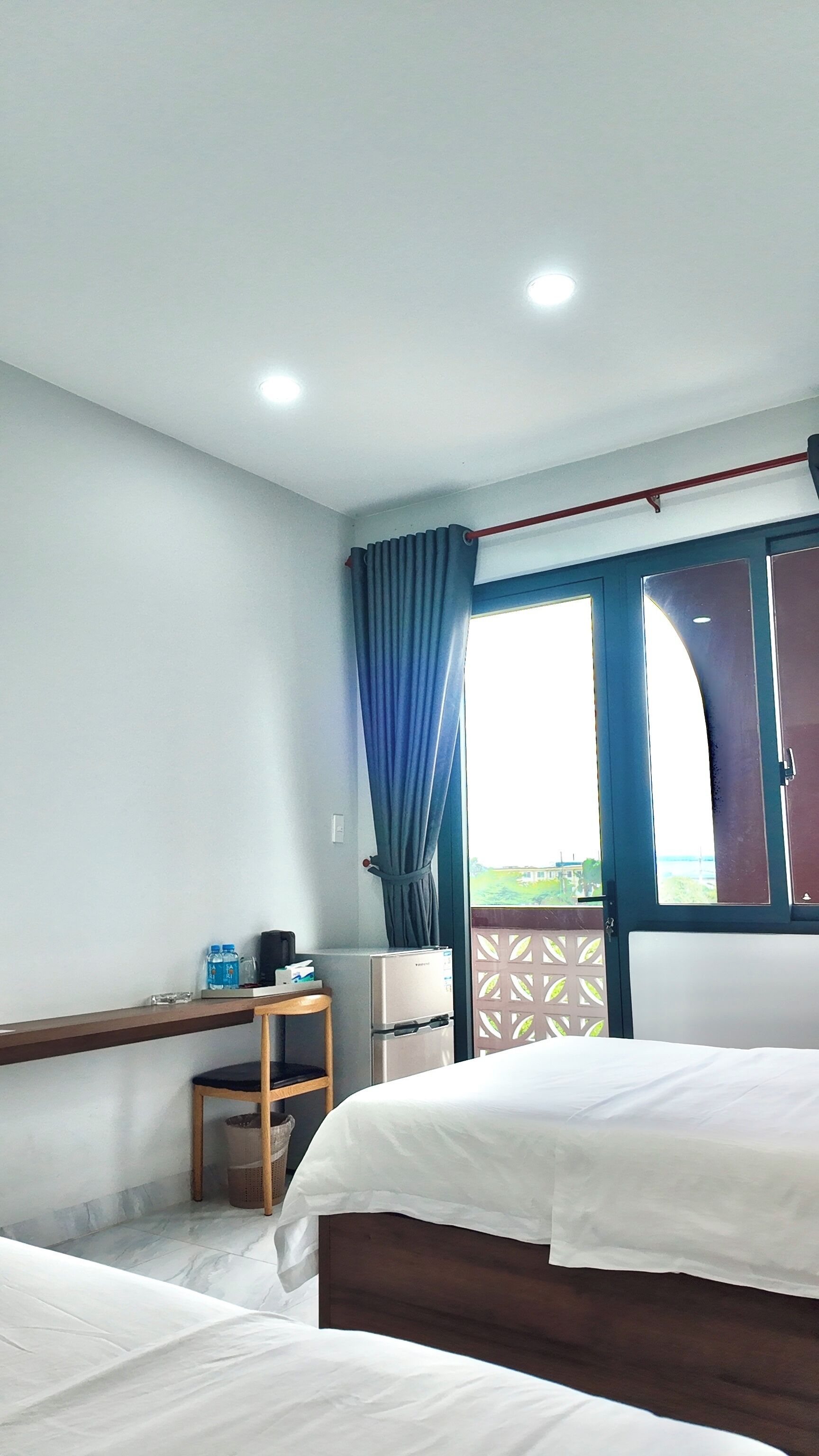 Ein Hotelzimmer mit zwei Betten, einem Schreibtisch, einem Kühlschrank und einem Fenster mit Vorhängen.