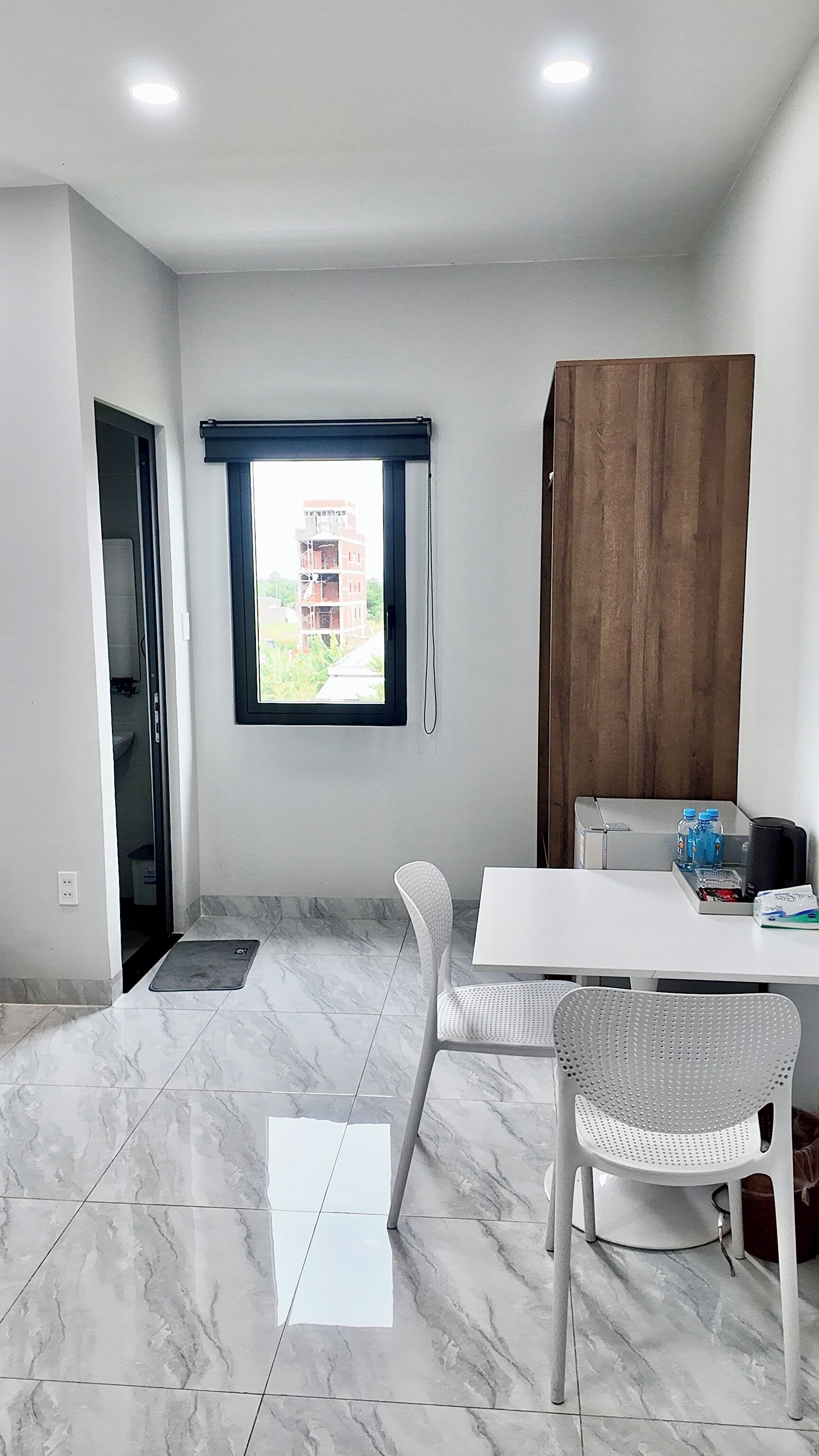 A room with a white table, a chair, a window with a view, and a wooden cabinet.
