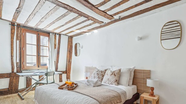 Ein Schlafzimmer mit Holzboden, einem Bett mit Kopfteil, einem Nachttisch mit Lampe und einem Fenster mit Vorhängen.