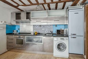 Eine moderne Küche mit Edelstahlgeräten, einem Einbauofen, einer Waschmaschine und einer blauen Spritzschutzwand.