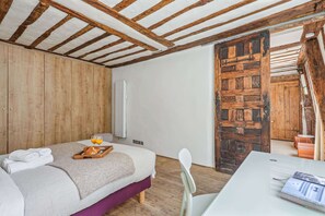 A bedroom with a wooden ceiling, a bed with a tray of croissants and glasses, a chair, and a table with a book. - Bright 1BR - Walk to Louvre - Opera (Paris)
