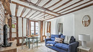 Ein gemütliches Wohnzimmer mit sichtbaren Holzbalken, einem blauen Sofa und einem Essbereich mit Tisch und Stühlen.