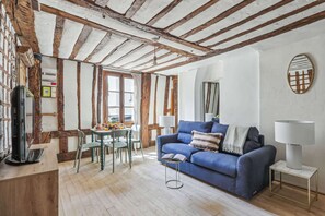 Ein gemütliches Wohnzimmer mit sichtbaren Holzbalken, einem blauen Sofa und einem Essbereich mit Tisch und Stühlen.