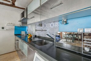 Eine moderne Küche mit Edelstahlgeräten, einer blauen Spritzschutzwand und einem Essbereich, der durch das Fenster sichtbar ist.