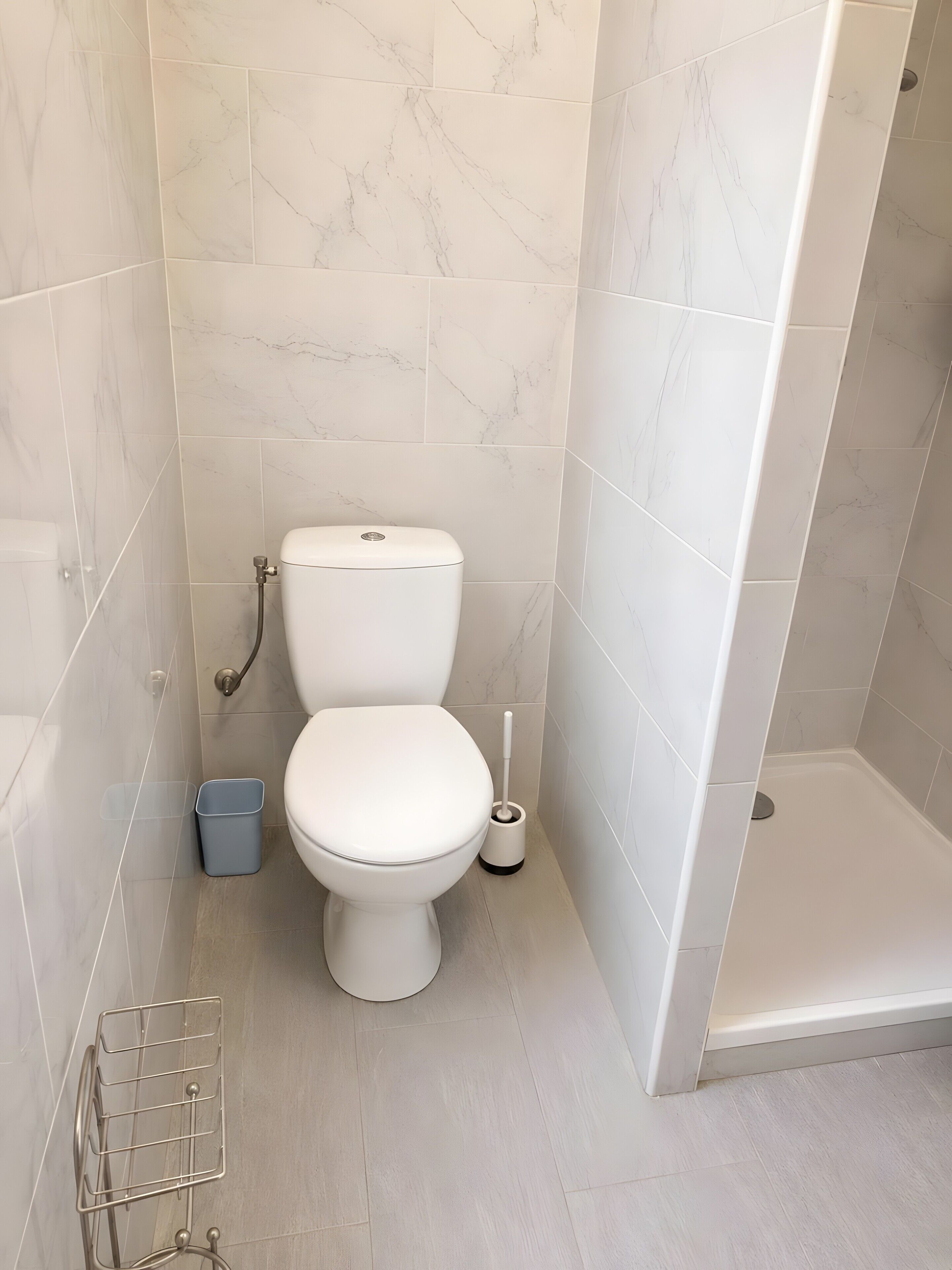 A bathroom with a toilet, a shower, and a waste bin.