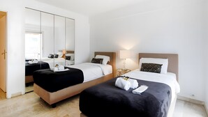 Een hotelkamer met twee bedden, een kledingkast, een spiegel en een nachtkastje met een lamp.