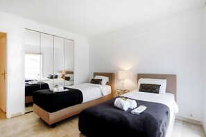 Ein Hotelzimmer mit zwei Betten, einem Kleiderschrank, einem Spiegel und einem Nachttisch mit Lampe.