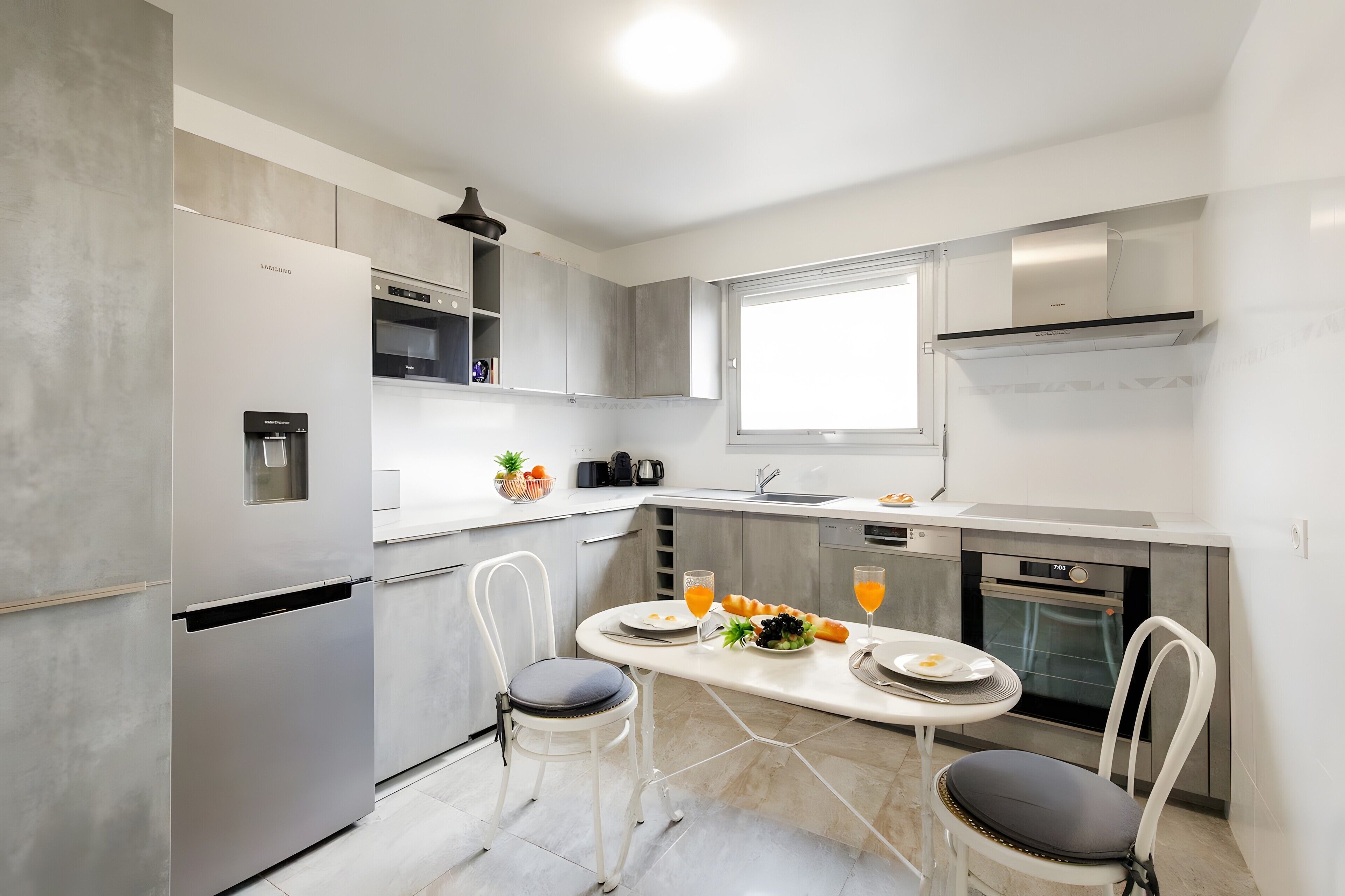 A modern kitchen with a built-in refrigerator, a microwave, and a stove. There is a dining table with chairs and a window above it.