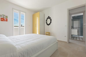 Ein Schlafzimmer mit einem Bett, einem gelben Kleiderschrank, einem Spiegel und Blick auf einen Balkon.