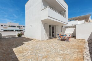 Edifici de dues plantes de color blanc amb un pati d'àmfores de pedra i una zona de menjador amb mobiliari exterior.